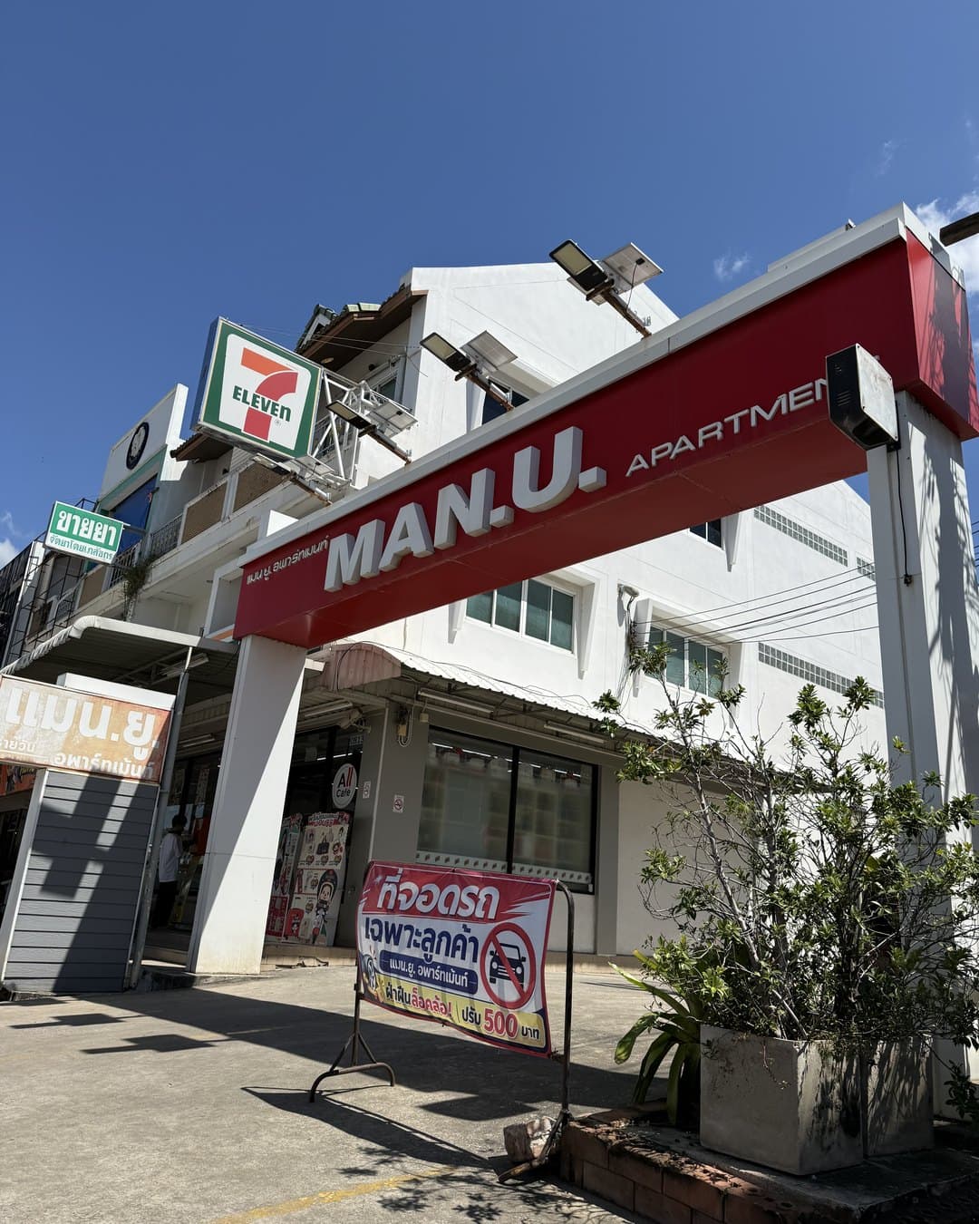 Eingang mit rotem Schild MAN.U. Apartment, links daneben ein 7-Eleven